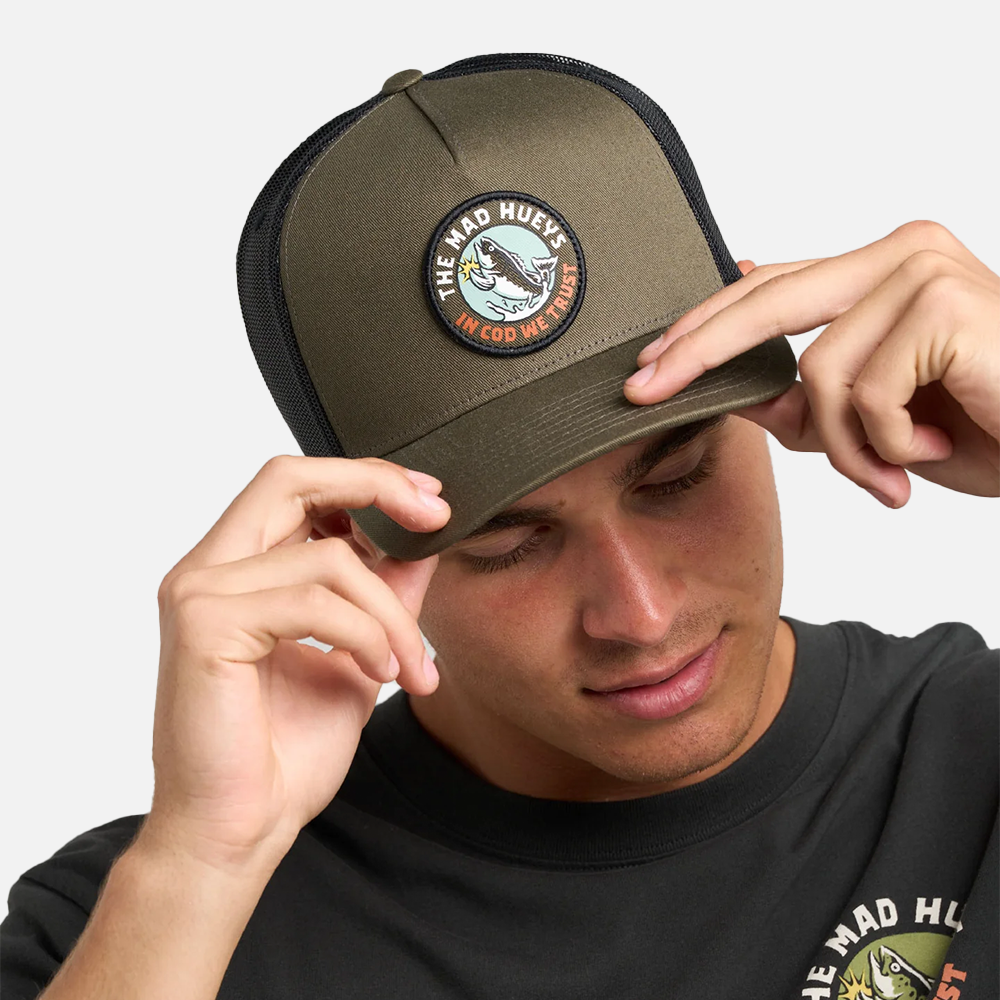 Person wearing a green cap with a logo, adjusting it on a plain background