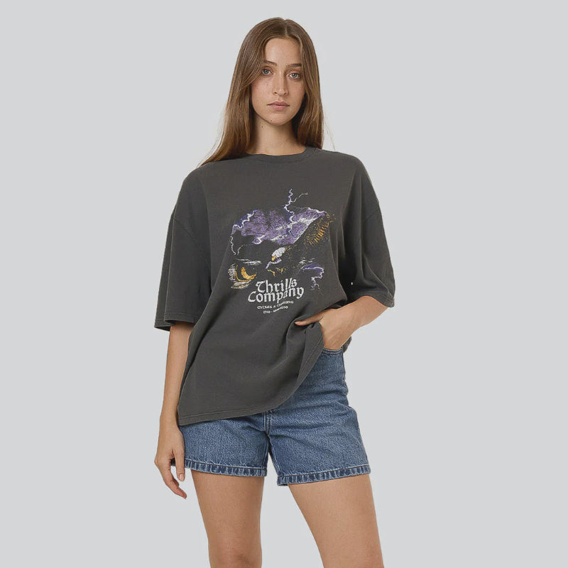Woman wearing a dark gray t-shirt with graphic design, denim shorts, and black boots on a light gray background