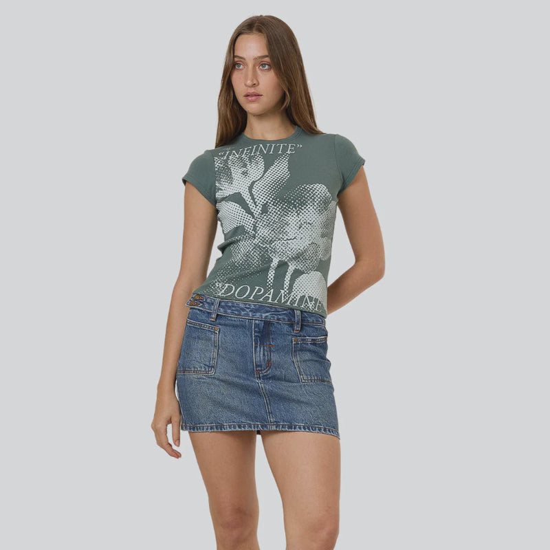 Woman wearing a green graphic t-shirt and denim skirt on a gray background