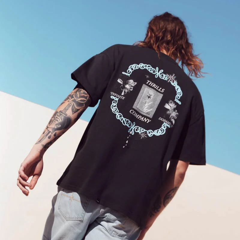 Person wearing a black t-shirt with a graphic design on the back, standing against a clear blue sky.