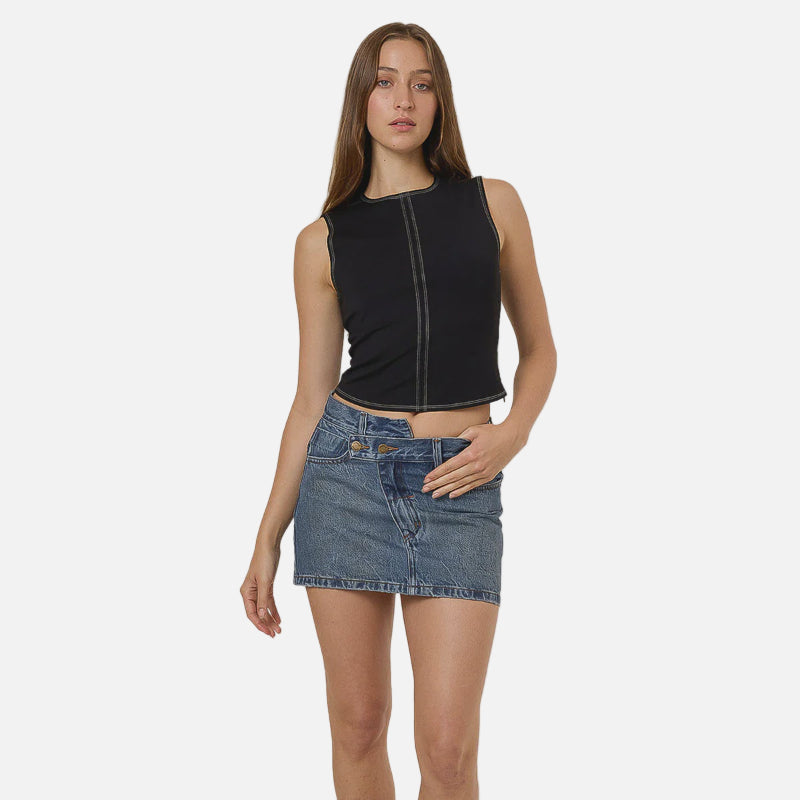 Woman wearing a black sleeveless top and denim skirt with black boots on a white background