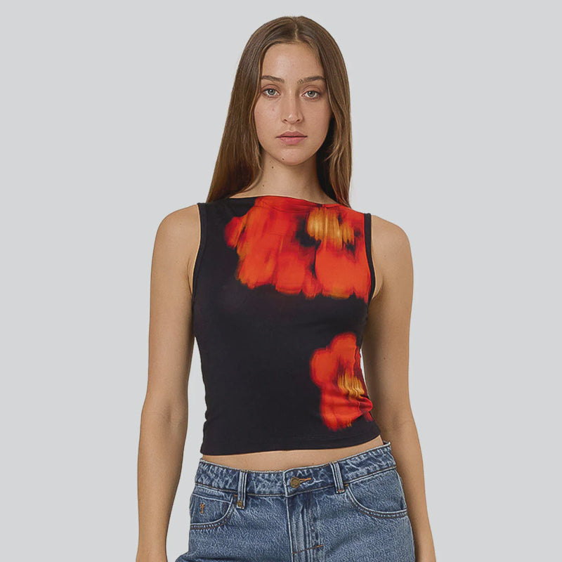 Woman wearing a black tank top with red and red flower design and blue jeans on a gray background