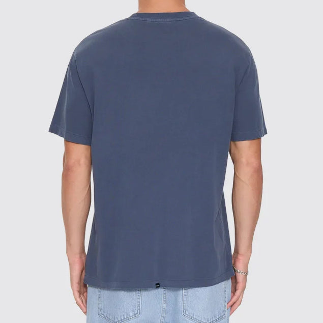 A man viewed from behind wearing a slate blue crewneck t-shirt and light wash jeans, standing against a solid light gray background.