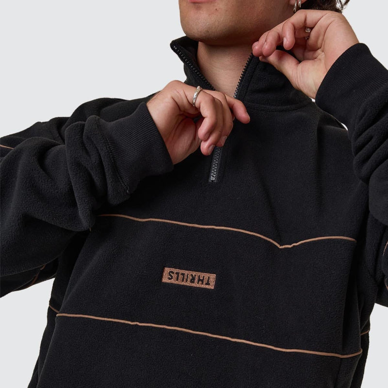 Person wearing a black fleece pullover with a brand logo on a light gray background