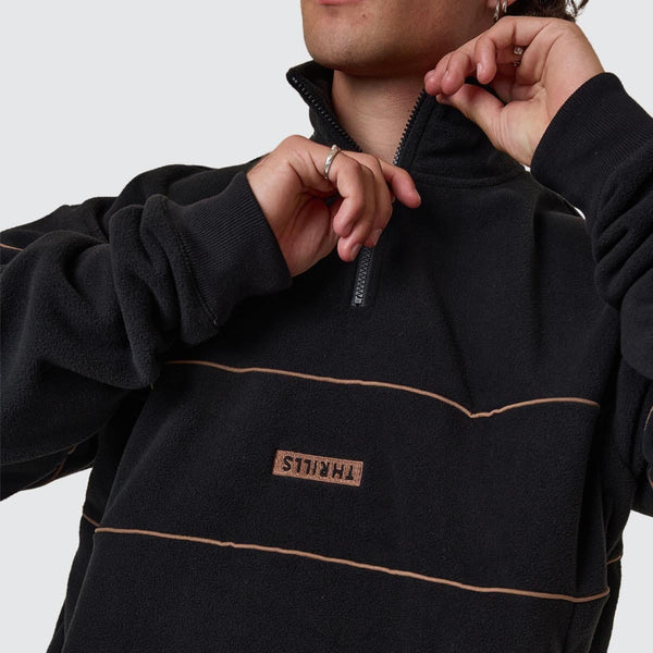 Person wearing a black fleece pullover with a brand logo on a light gray background