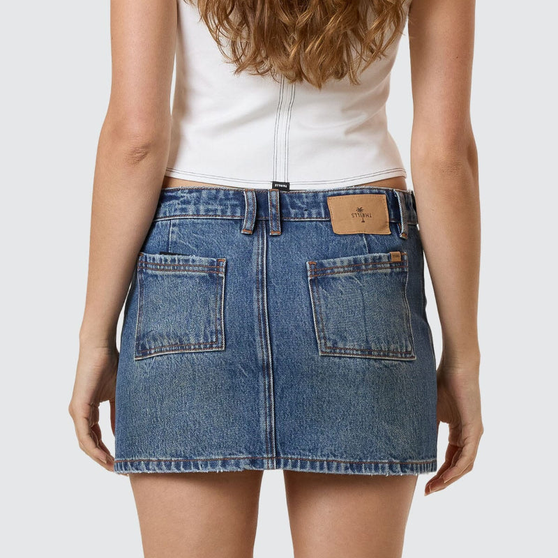 Person wearing a blue denim skirt with a white top on a plain background