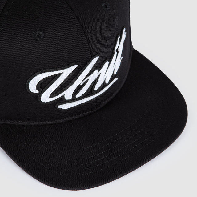 A close-up shot of a black snapback cap featuring a white embroidered script logo on the front panel, set against a light gray background.