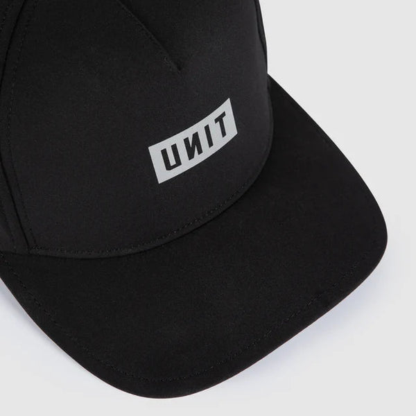 A close-up of a black baseball cap with a white rectangular patch on the front displaying the brand name 'UNIT' in black letters, set against a light gray background.