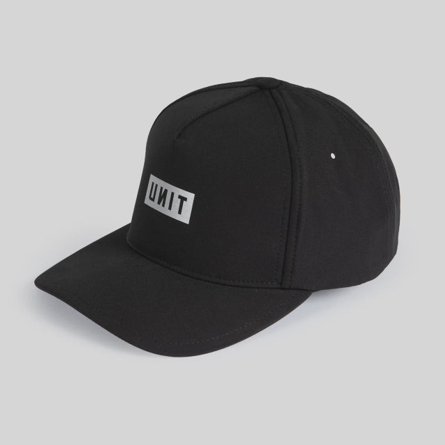 A black structured baseball cap with a white rectangular patch on the front displaying the word 'UNIT' in black capital letters, photographed on a light gray background.