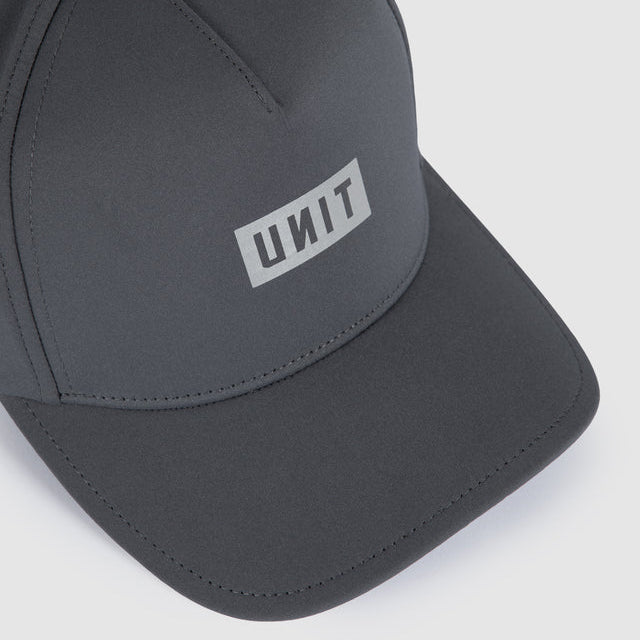 A dark gray baseball cap with a white rectangular logo patch on the front displaying the text 'UNIT' in reverse, photographed on a light gray background.