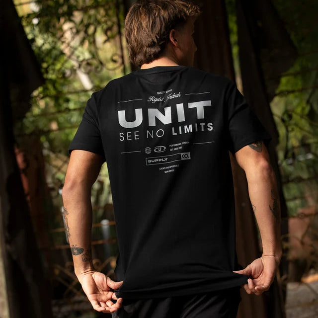 A man wearing a black t-shirt with a white graphic print on the back, standing outdoors in a wooded area.