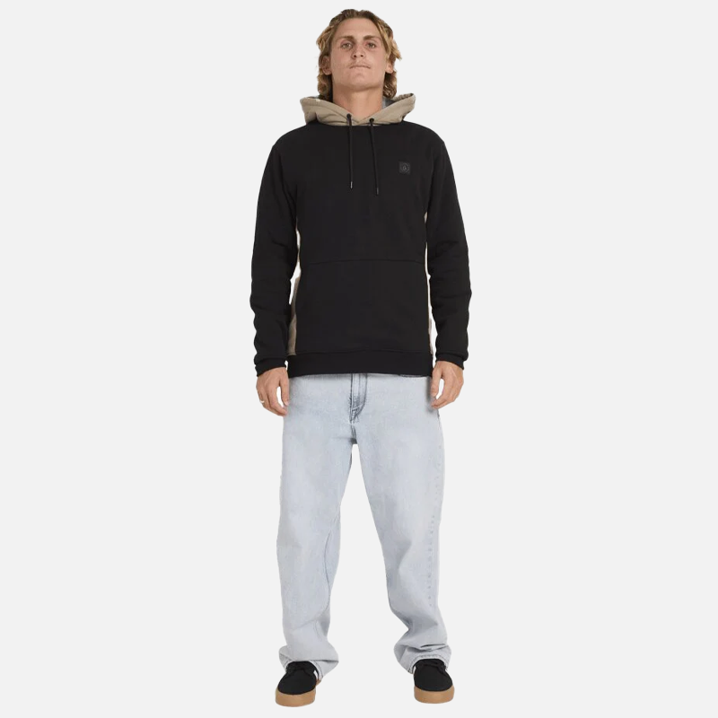 Man wearing a black hoodie with a beige hood and light blue jeans on a white background