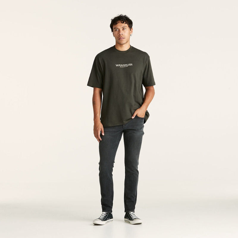 Man wearing a dark green Wrangler t-shirt and jeans on a white background